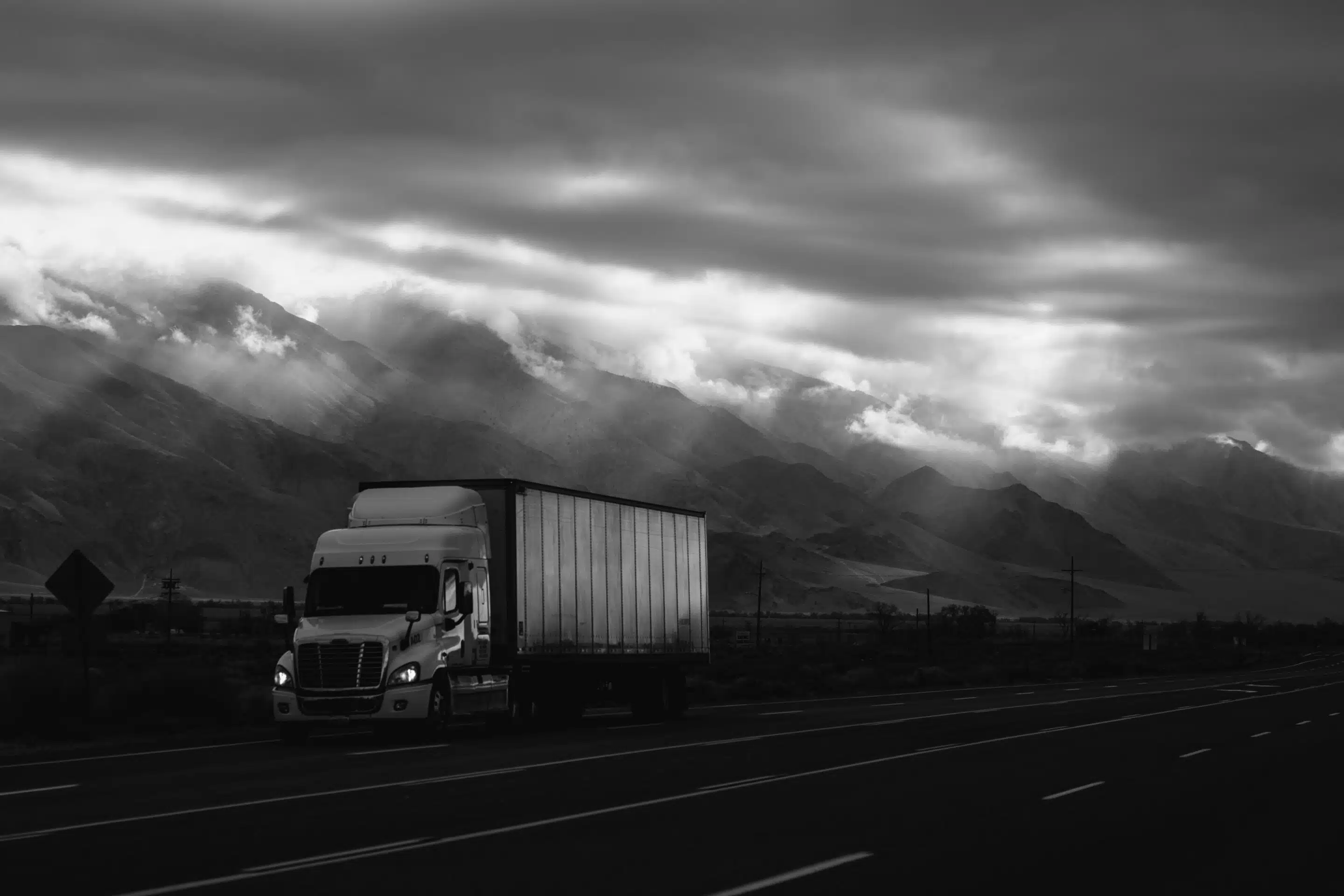 Black and white photo of semi driving in mountains.